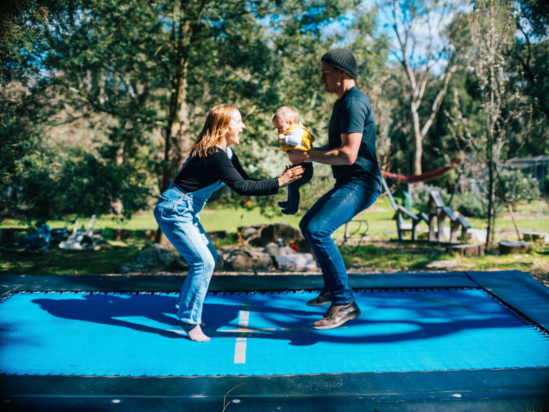 Rachel and Ollie bouncing on the trampoline together holding their baby between them
