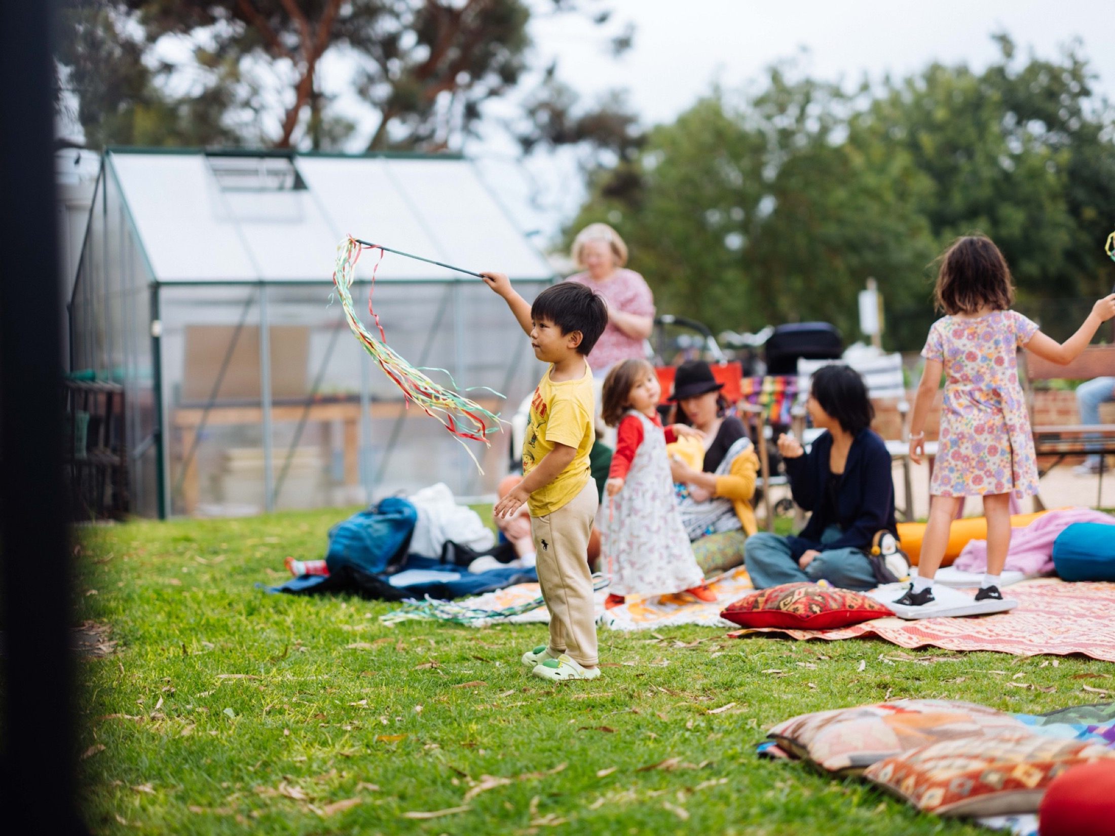 A young child dancing with ribbon streamers on the grass while families sit on rugs behind